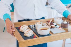 Ein Kellner serviert eine Holztablett mit verschiedenen Desserts und Speisen im Iberostar Selection Playa de Palma Hotel.