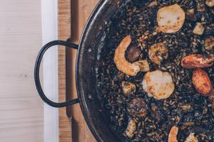 Nahaufnahme einer Paella in einer Pfanne mit Garnelen, Muscheln und Tintenfisch auf einem Holzbrett
