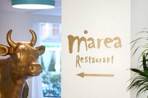 Eingang zum Marea Restaurant mit goldener Kuh Statue und grüner Pflanze.