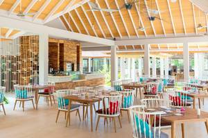Innenbereich des Dhigali Maldives Hotels mit Holztischen, Stühlen und Deckenventilatoren.