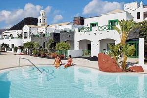 Zwei Gaeste sitzen im Pool des LIVVO Volcan Lanzarote Hotels vor weissen Gebaeuden.