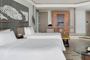 Zimmer im Shangri-La Le Touessrok Hotel mit zwei weißen Betten, Tisch, Fernseher und üppiger Einrichtung.