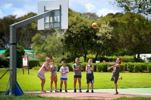 Kinder spielen Basketball am VOI Alimini Resort während eine Frau den Ball wirft.