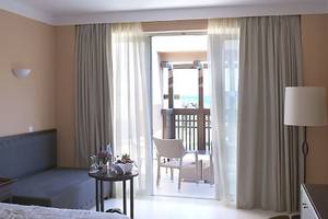 Hotelzimmer des Atlantica Belvedere Resort mit Balkon, Bett, Sessel und Fernseher.
