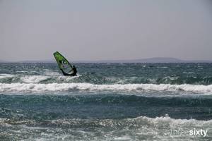 Eine Person windsurft in stürmischem Ozean mit hohen Wellen.