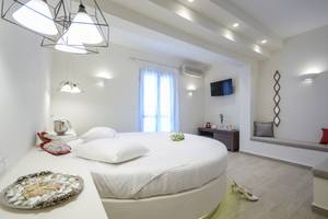 Schlafzimmer im Alkyoni Beach Hotel mit rundem Bett, weißen Kissen und Dekor.