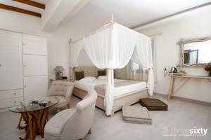 Schlafzimmer im Alkyoni Beach Hotel mit Baldachinbett, zwei Sesseln, Glastisch und Dekor.