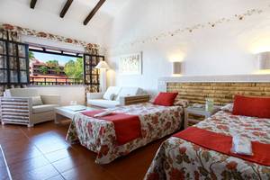 Doppelzimmer im Parque Tropical Hotel mit zwei Betten, roten Kissen und einem Wohnzimmerbereich.