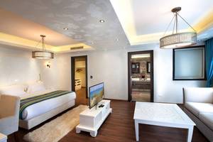 Hotelzimmer im Sunrise Arabian Beach Resort mit großem Bett, Fernseher, Tisch, Couch und modernen Möbeln.