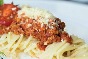 Gewürzte Spaghetti mit Fleischsoße und Käse auf einem weißen Teller serviert