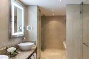 Badezimmer des Sheraton Oman Hotels mit Waschbecken, Spiegel und begehbarer Dusche.
