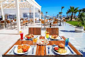 Außenbereich des Pickalbatros Royal Moderna Resorts mit Tisch und Essen, umgeben von Palmen und Blick auf den Strand.