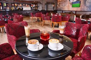 Loungebereich des Pickalbatros Royal Moderna Resort mit rot gepolsterten Stühlen und Kaffeespezialitäten auf dem Tisch.