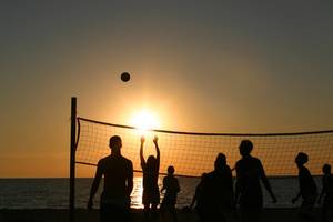 Gruppe von Menschen spielt Volleyball am Strand während des Sonnenuntergangs.