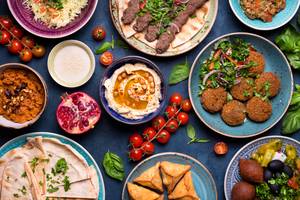 Orientalische Gerichte wie Falafel, Hummus und verschiedene Salate auf einem blauen Hintergrund.