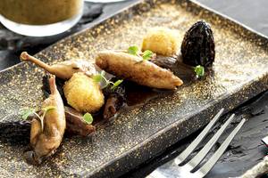 Eine goldglänzende Platte mit verschiedenen Gerichten wie gebratenen Entenbeinen, gedünsteten Früchten und Sauce, serviert im Myconian Villa Collection Hotel.
