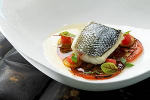 Ein Fischgericht in einem weißen Teller mit Tomaten und grünen Blattgemüse