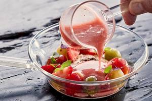 Ein Glas mit gemischten Früchten und rosa Soße wird auf einem dunklen Tisch serviert.