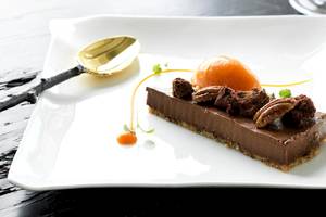 Schokoladen Tarte auf einem weißen Teller mit einem goldenen Spatel.
