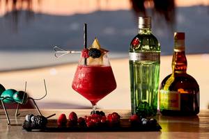 Cocktail auf einem Tisch mit einer Ameisenskulptur, Gin und anderen Getränken im Hintergrund.