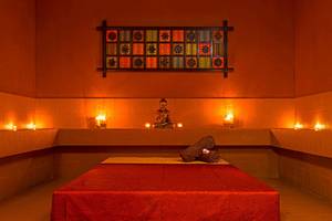 Spa-Zimmer im Le Meridien Abu Dhabi mit Buddha-Statue, Kerzen und rotem Bett.