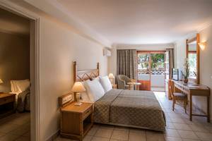Schlafzimmer im Mitsis Petit Palais Beach Hotel mit Bett, Schreibtisch und Balkon.