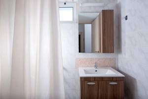 Badezimmer im Gouves Water Park Holiday Resort mit weißen Fliesen, braunem Schrank und einem Spiegel.
