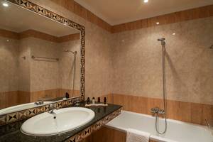 Badezimmer im Mitsis Petit Palais Beach Hotel mit Badewanne, Waschbecken und Spiegel.