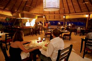 Ein Paar sitzt bei einem Tisch im Innenbereich des Kuredu Island Resorts und Spa, bei Nacht.