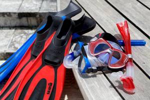 Schnorchelausrüstung wie Maske, Schnorchel und Flossen auf einer Holzbank.