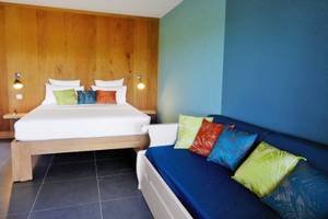 Schlafzimmer im Aparthotel Le Panoramic mit blauer Wand, Holzbett und Sofa.