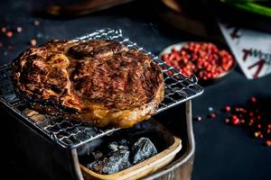 Ein Steak auf einem Grillrost mit Raucheffekten auf einem schwarzen Hintergrund.
