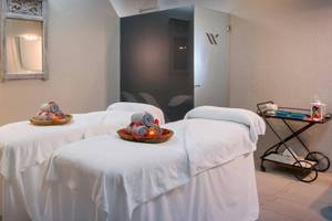 Massageraum im Barcelo Corralejo Bay Hotel mit zwei Massagetischen, Kissen und Kerzen.