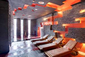Saunabereich im Barcelo Corralejo Bay Hotel mit roten und schwarzen Wandverkleidungen und cremefarbenen Liegen.