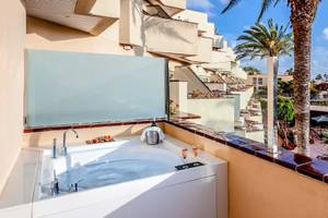 Balkon mit Whirlpool im Barcelo Corralejo Bay Hotel mit Blick auf Palmen und Gebäude.