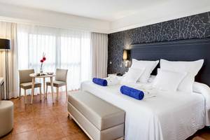 Zimmer im Barcelo Corralejo Bay Hotel mit Bett, Tisch, Stühlen und Dekor.