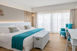 Innenansicht eines Hotelzimmers mit Bett, Kissen, Tisch, Stuhl und Fernseher.