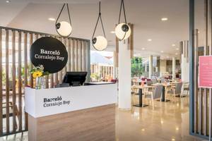 Innenansicht der Rezeption des Barcelo Corralejo Bay Hotels mit Tisch, Stühlen und Schildern.