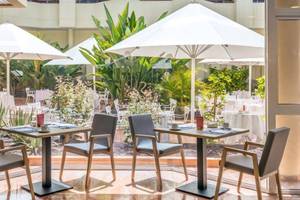 Gartenbereich des Barcelo Corralejo Bay Hotels mit Tischen, Stühlen und Schirmen.