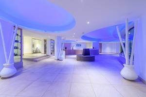 Lobbybereich des Asterias Beach Hotels mit hellen Fliesen, violetten Lichtern und Empfangstresen.