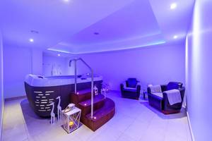 Jacuzzi-Raum im Asterias Beach Hotel mit lila Beleuchtung und zwei Lounge-Sesseln.