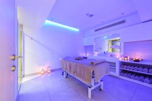Spa-Behandlungsraum im Asterias Beach Hotel mit violettem Licht und weißen Fliesen.