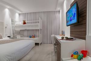 Inneneinrichtung eines Zimmers im Asterias Beach Hotel mit zwei Betten, einem Fernseher, und Spielzeug.