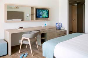 Innenansicht eines Zimmers im Asterias Beach Hotel mit Schreibtisch, Stuhl, Fernseher und Bett.