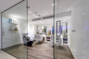 Innenansicht des Friseursalons im Asterias Beach Hotel mit Glaswänden, Holzboden und weißen Möbeln.