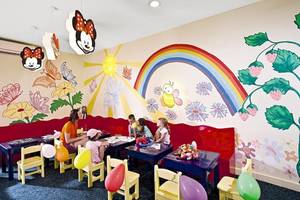 Spielzimmer im Serenity Alma Heights Hotel mit bunten Wandmalereien, bunten Stühlen und Tischen, Luftballons und einer Frau, die Kindern hilft.