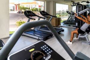Fitness-Center im Serenity Alma Heights Hotel mit mehreren Laufbändern und einem Mann, der an einem Gerät trainiert.