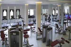 Fitnessstudio im Salalah Rotana Resort mit diversen Geräten und einer Frau auf dem Fernsehbildschirm.