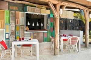 Außenbereich des Zilwa Attitude Hotels mit bunten Fensterläden und Tischen und Stühlen auf weißem Sand.