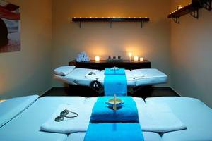 Behandlungsraum im Michelangelo Resort & Spa mit zwei Massageliegen und blauen Handtüchern.